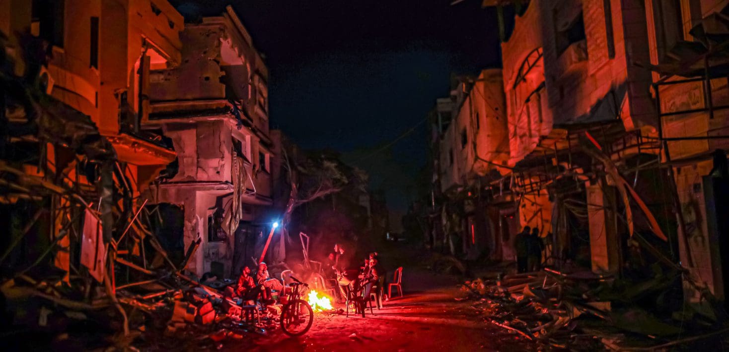 a small fire burns in the middle of a devastated Gaza street