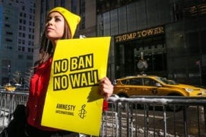 A wona protester holding a "No Ban No Wall" sign in front of Trump Tower