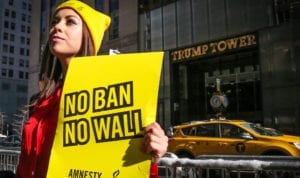 A wona protester holding a "No Ban No Wall" sign in front of Trump Tower