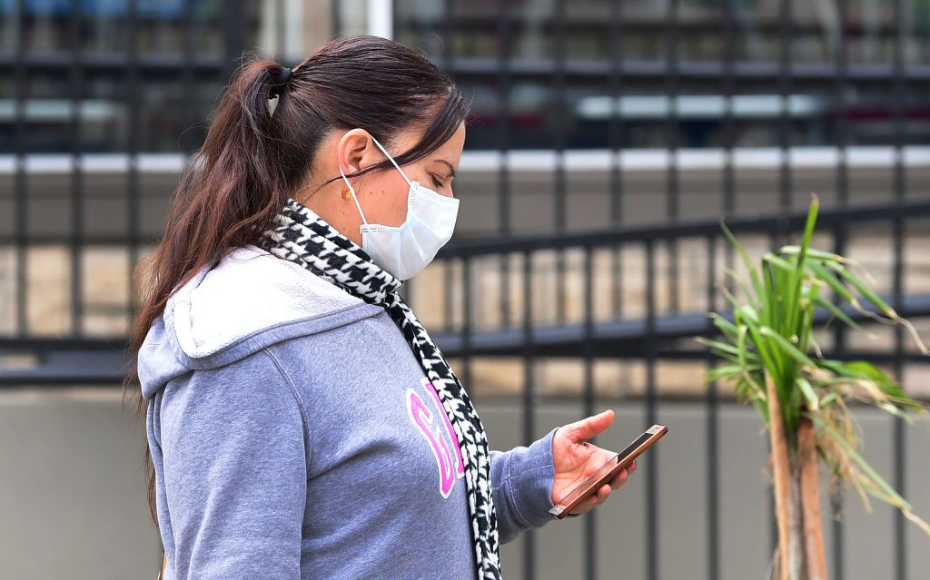 Woman wearing a facemark during COVID-19 pandemic looks at the cell phone in her hand