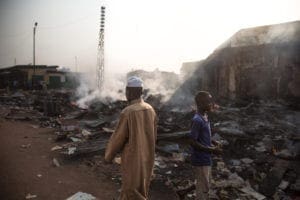 Two people walk among the burning rubbles