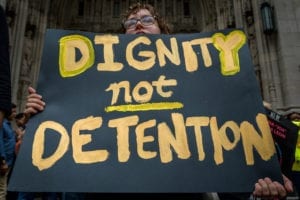 Protestor holds sign, "dignity not detention"