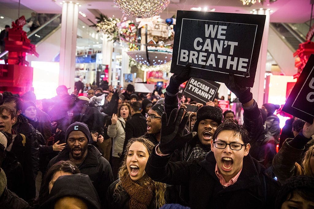 Large group of black and white people hold signs, reading