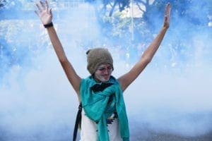 Woman holds her hands up with her eyes closed while gas surrounds her