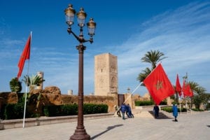 Three men hold up the Moroccan flag as other men stand behind them in front of a tall tower