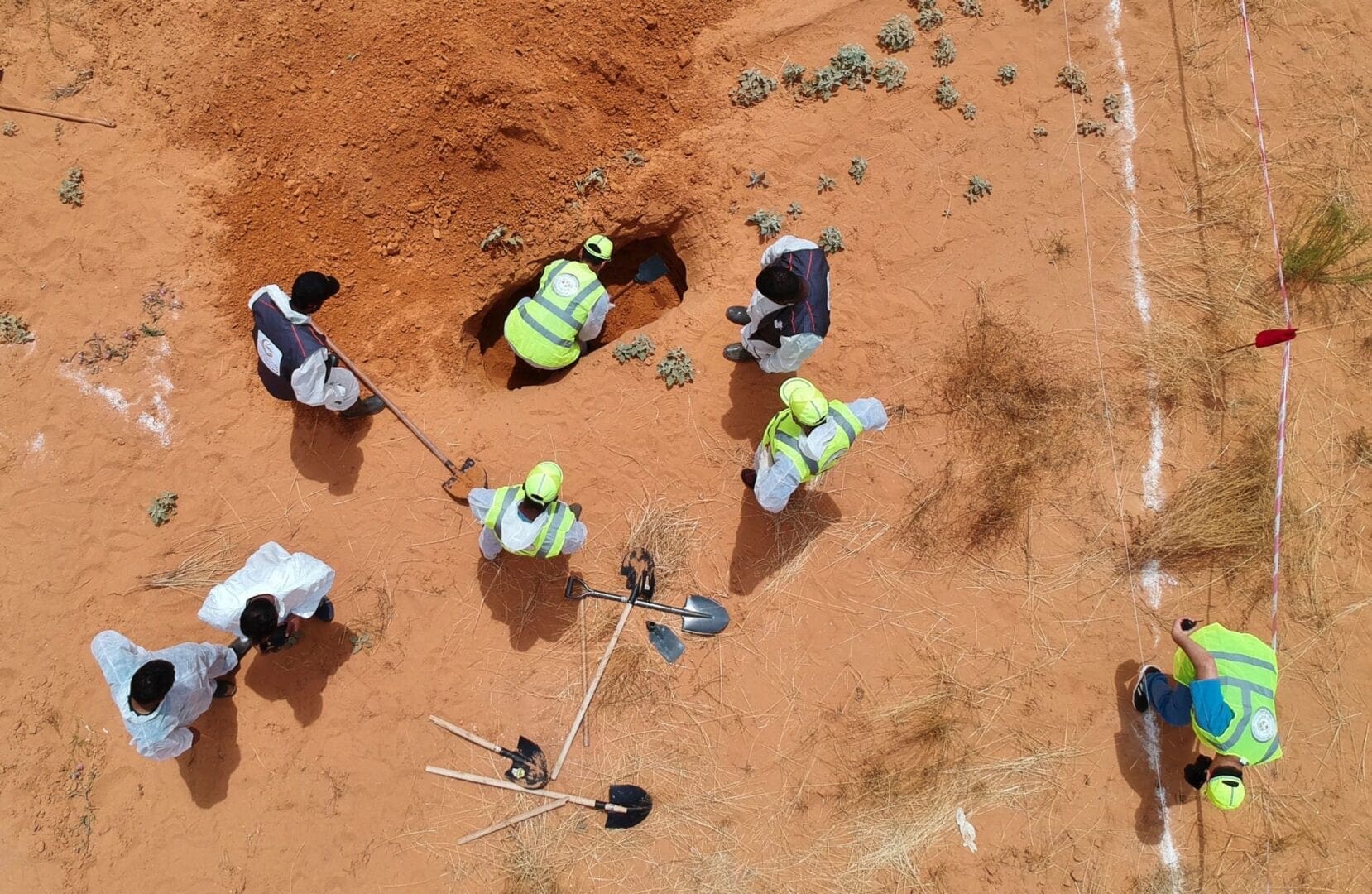 6 men stand around a grave with shovels