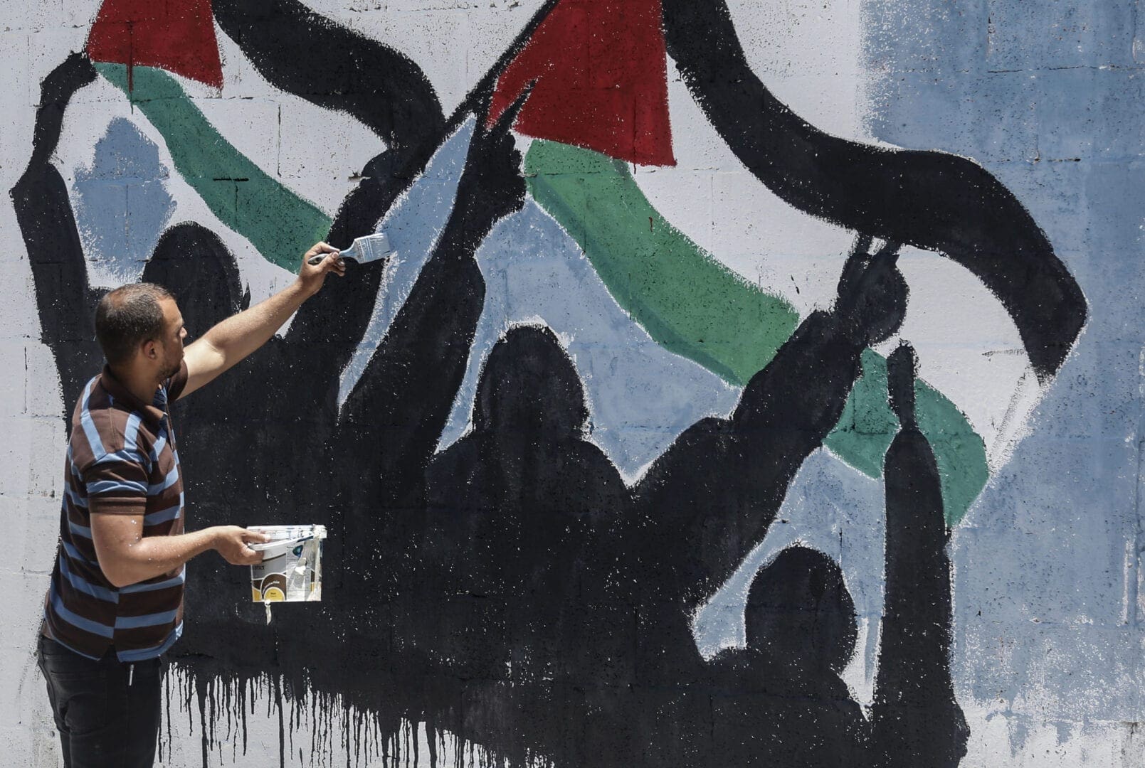 Man holds brush and pains a mural of a flag