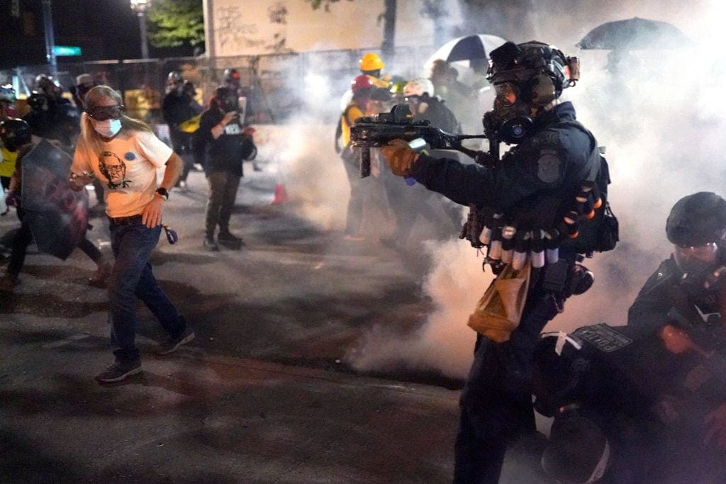 PORTLAND, OR - JULY 30: A federal officer points his less-lethal weapon into the crowd while dispersing a protest against racial injustice and police brutality in front of the Mark O. Hatfield U.S. Courthouse in the early hours of July 30, 2020 in Portland, Oregon. Protests against the federal presence in Portland continued Wednesday following an announcement by Governor Kate Brown that federal officers would begin a phased withdrawal from the city. (Photo by Nathan Howard/Getty Images)