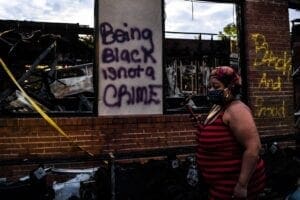 Woman walks past a wall on which graffitti reads "Being Black is not a CRIME"