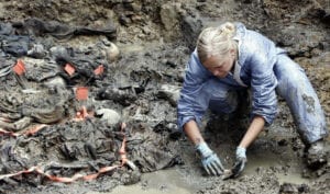 Woman bends down to excavate the mass grave filled with bones around her
