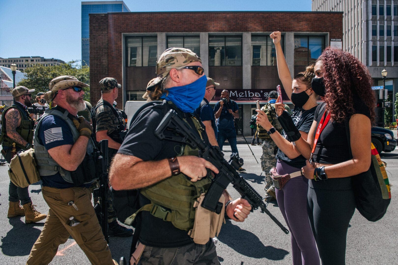Women stand in the street unarmed as right-wing protesters stand across them, armed