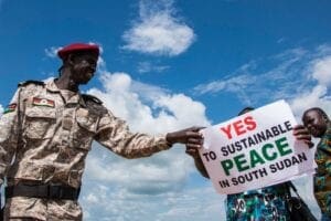 Civilian holds sign that says "yes to sustainable peace in South Sudan" in front of a security officer