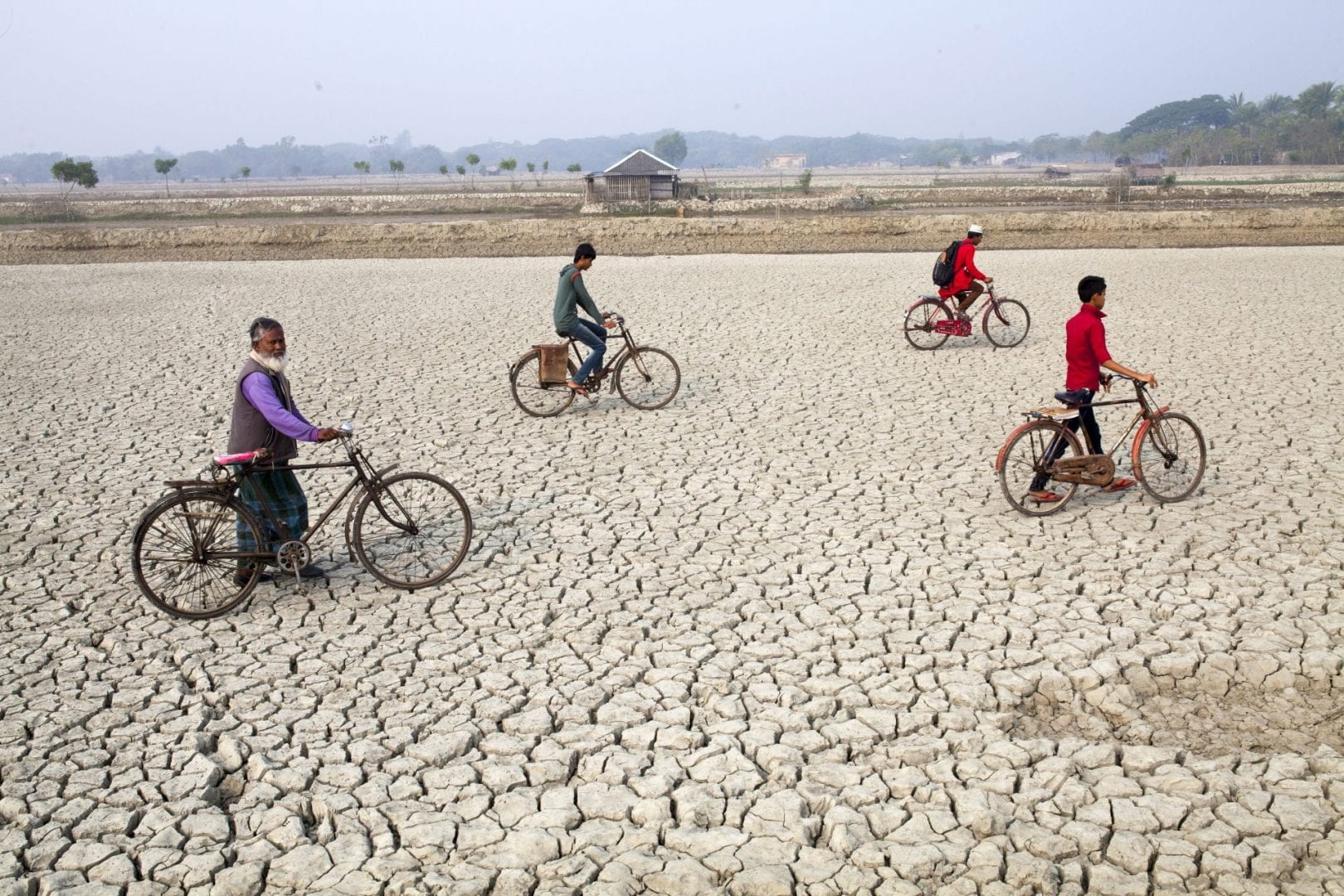 4 villagers on bicycles seen on a dried river bed