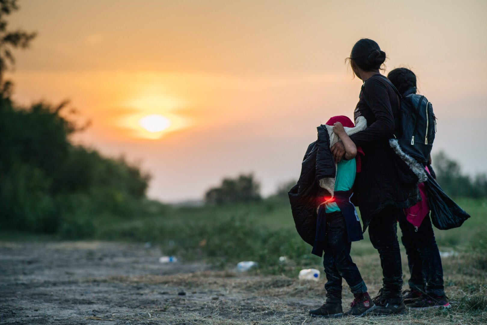 A migrant family watches the sunset while waiting to be accounted for and taken to a border patrol processing facility after crossing the Rio Grande into the U.S. on June 21, 2021 in La Joya, Texas. A surge of mostly Central American immigrants crossing into the United States has challenged U.S. immigration agencies along the U.S. Southern border.