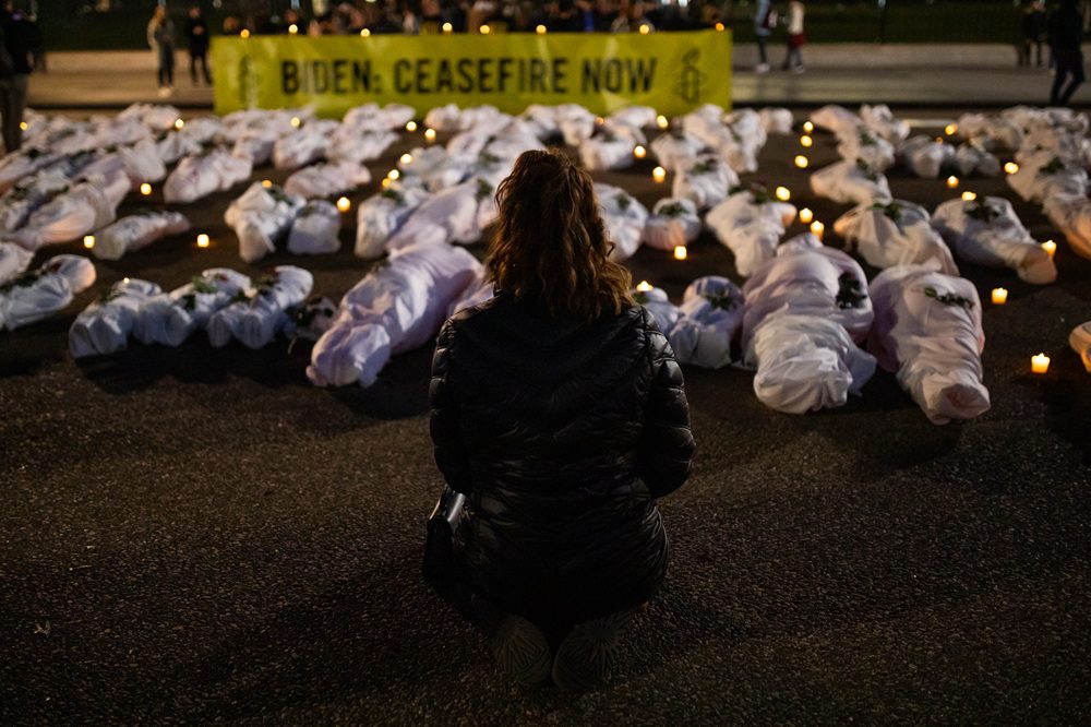 Woman crouches in front of candlelit vigil at Ceasefire Now demonstration at White House
