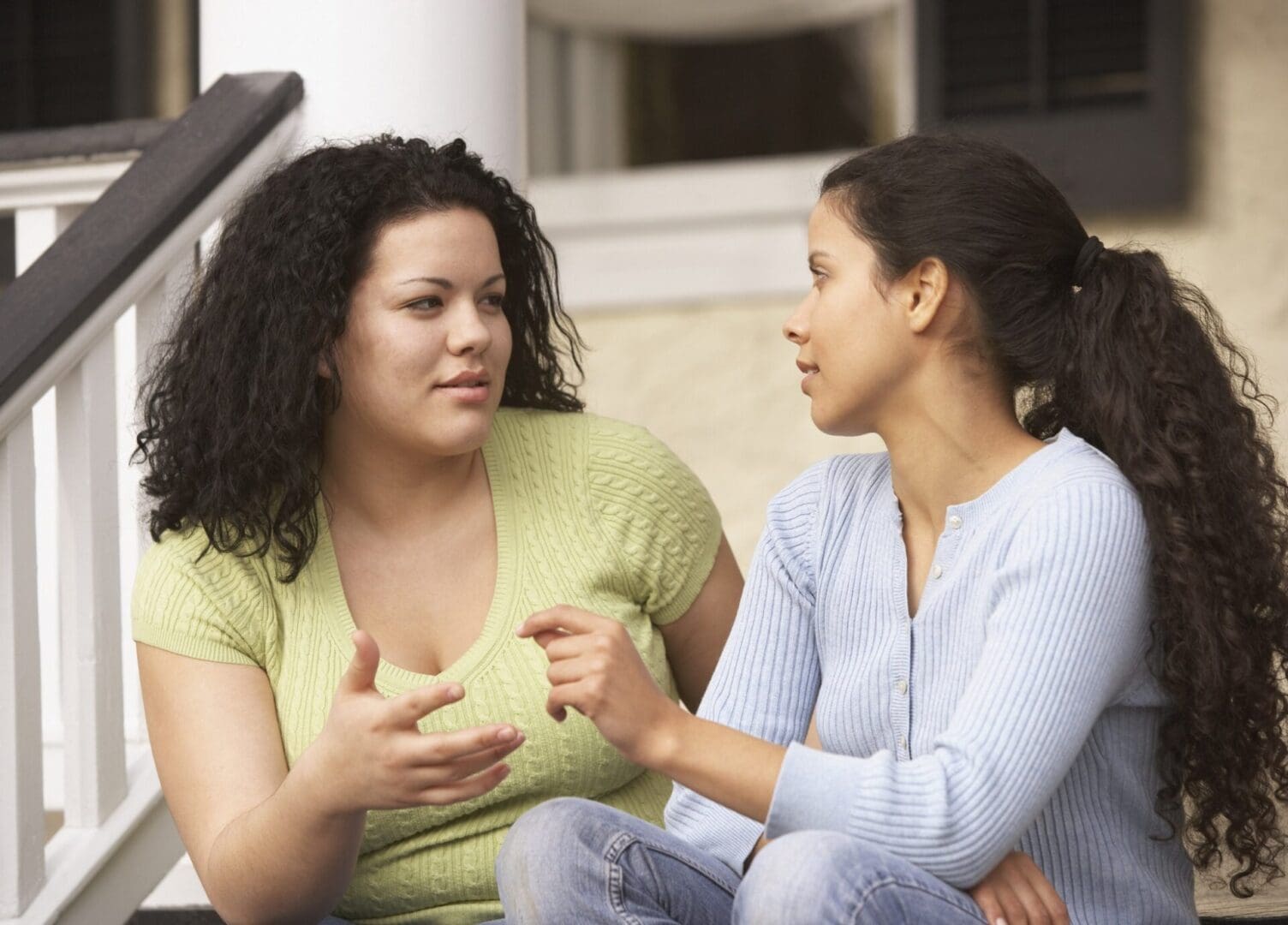 Hispanic sisters sitting on the porch talking