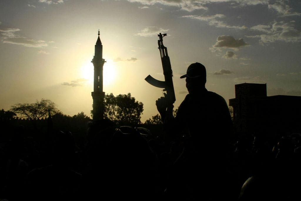 TOPSHOT - A fighter loyal to Sudan's army chief Abdel Fattah al-Burhan holds up a weapon backdropped by the minaret of a mosque, during a graduation ceremony in the southeastern Gedaref state on May 27, 2024. Sudan has been in the throes of conflict for over a year between the regular army led by de facto ruler Abdel Fattah al-Burhan and the RSF led by his former deputy Mohamed Hamdan Daglo. (Photo by AFP) (Photo by -/AFP via Getty Images)
