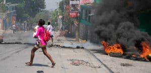 Woman carrying child walking across street with burning tires
