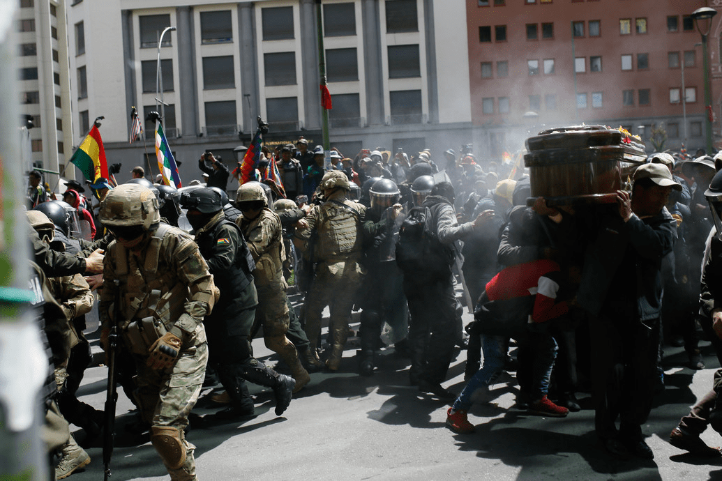 LA PAZ, BOLIVIA - NOVEMBER 21: Police officers spray tear gas as a group of people carry a coffin of one of the victims killed during clashes with police at the Senkata fuel plant, during a funeral procession as demonstrators slash with the police on November 21, 2019 in La Paz, Bolivia. Police and military forces on Tuesday escorted gasoline tankers from a major fuel plant of YPFB in Senkata that had been blockaded for five days by Evo Morales' backers and at least eight people were reported killed during the operation. Opposition accuses Evo Morales of instigating and planning blockades of food and fuel. Street violence has killed 32 people since a disputed October 20 vote.