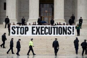 Protesters on the steps of the US capitol building hold a large banner which says in black letters STOP EXECUTIONS, while uniformed police circle around them.