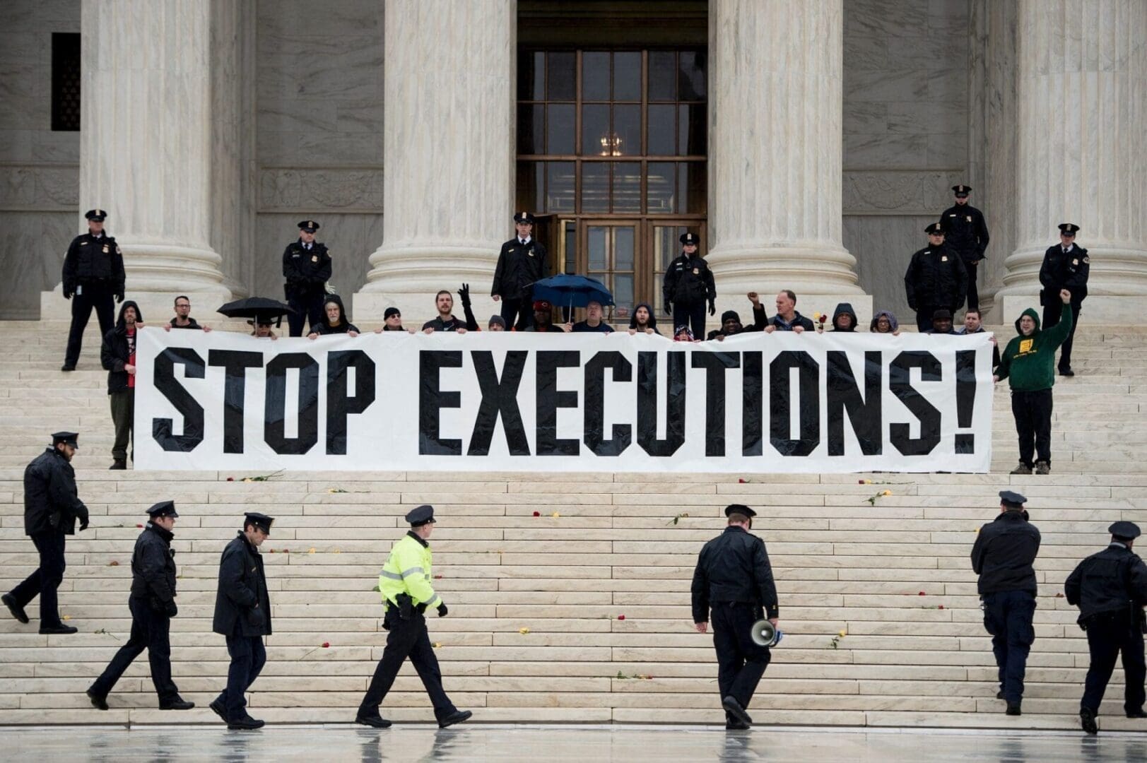Protesters on the steps of the US capitol building hold a large banner which says in black letters STOP EXECUTIONS, while uniformed police circle around them.