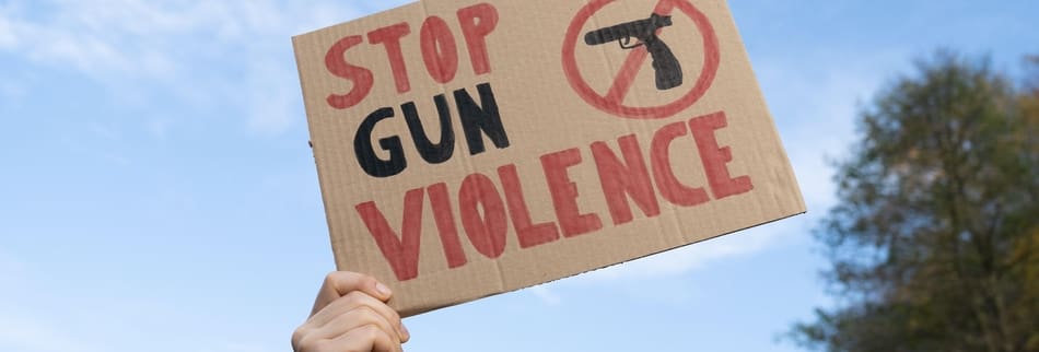 Hand holding sign with slogan Stop Gun Violence, black pistol strikethrough. Protest rally demonstration placard, strike to ban weapons, end shooting.