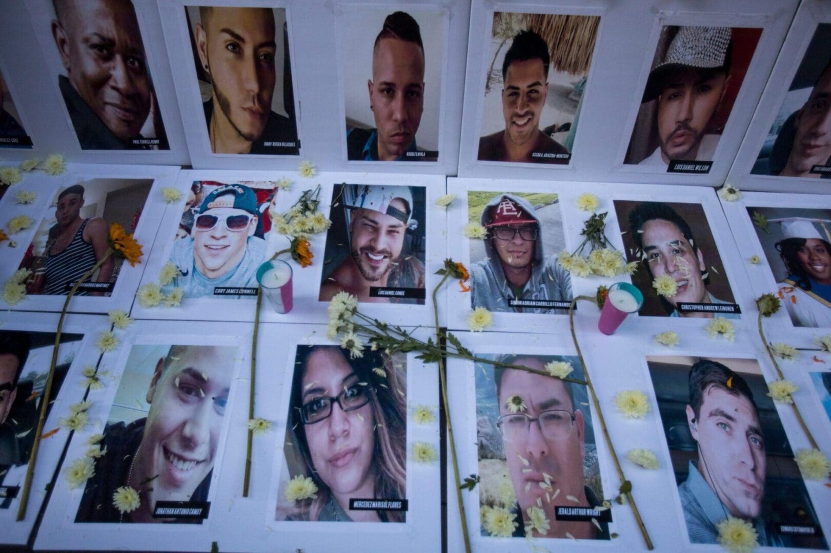 A memorial displays photos of victims of the Pulse nightclub shooting, strewn with small yellow flowers.