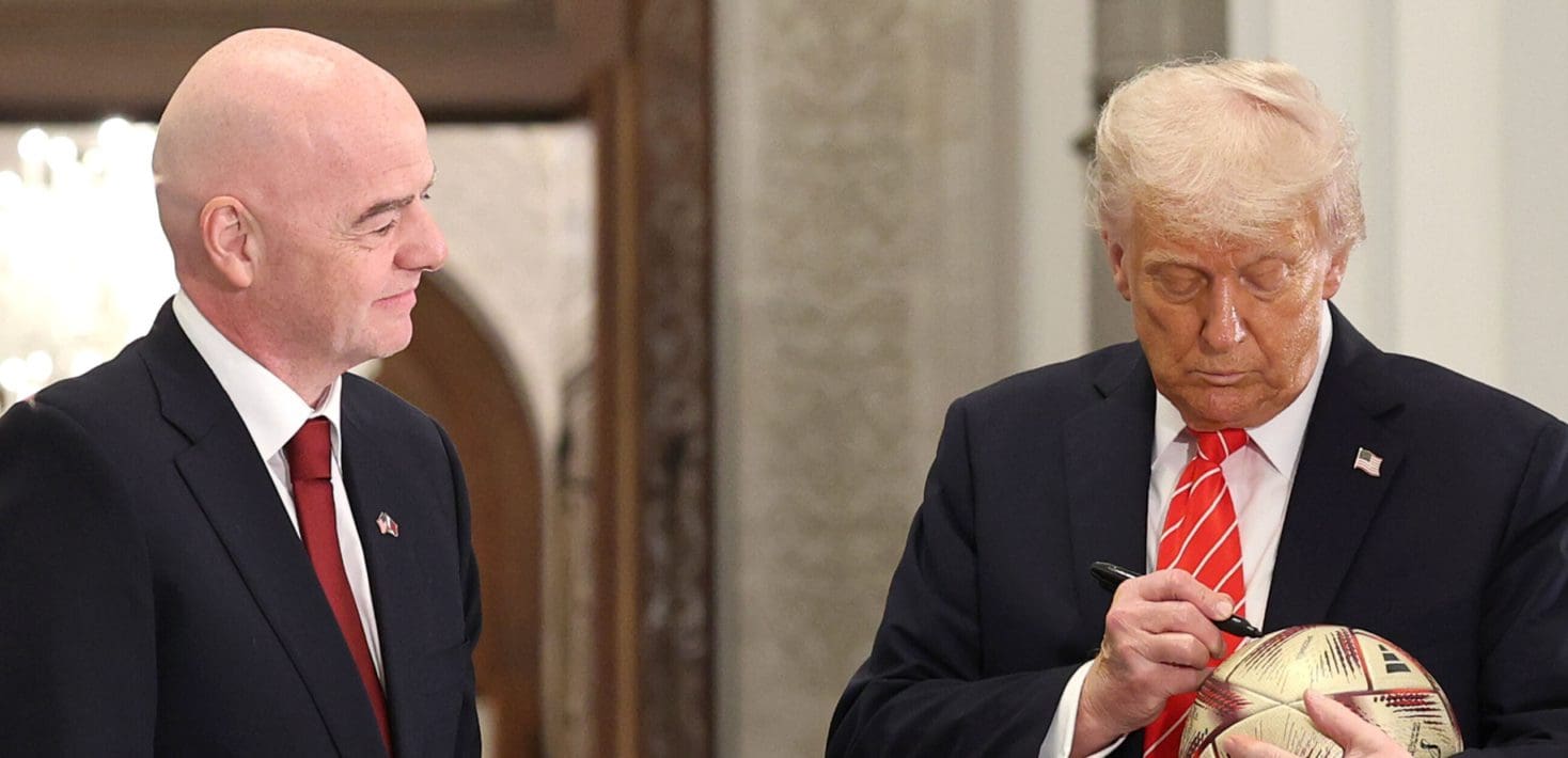FIFA President Gianni Infantino, wearing a suit, watches US President Donald Trump, also wearing a suit, sign a soccer ball.