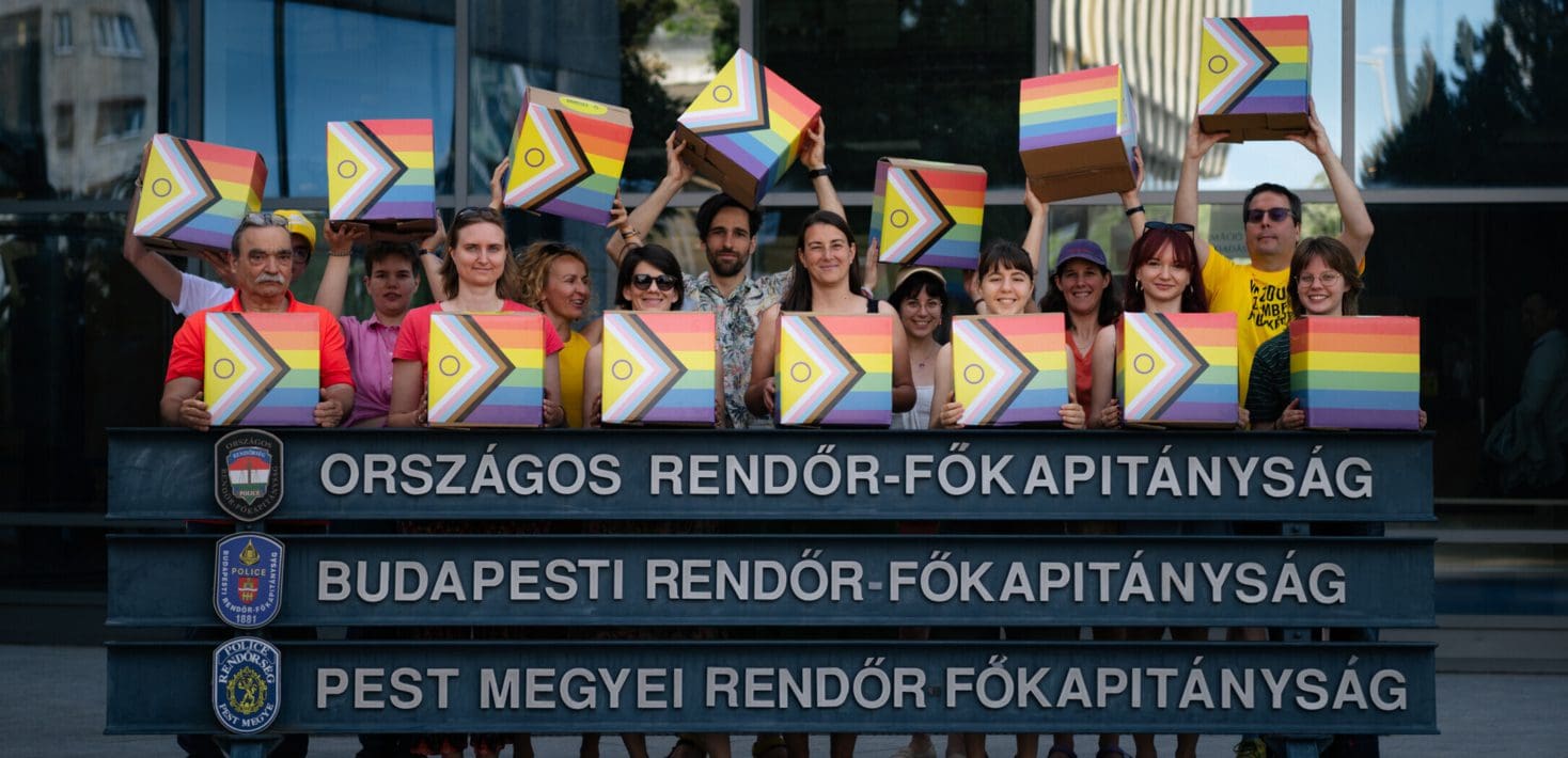 A group of people hold rainbow colored boxes behind a sign outside the police headquarters in Budapest, Hungary.