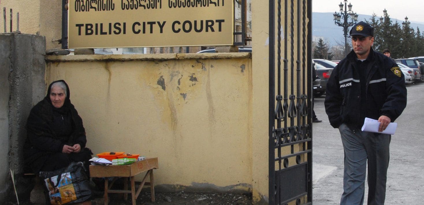 A man in uniform walks by a gate next to a sign that says Tblisi City Court.