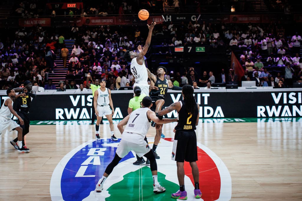 Two basketball teams jump for the ball on a Basketball Africa League court with Visit Rwanda advertisements behind them.
