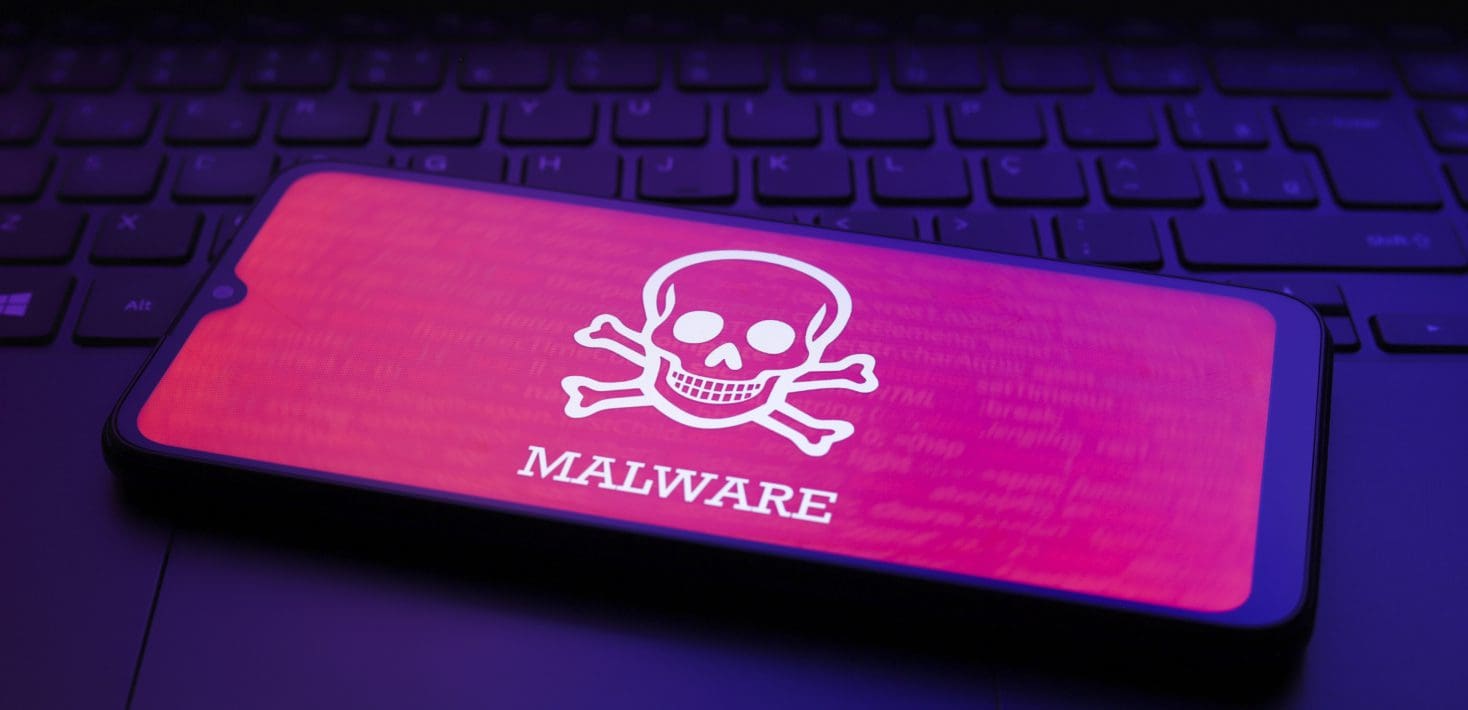 A cell phone sits on a darkened keyboard with a pink screen displaying a white skull and crossbones and the word