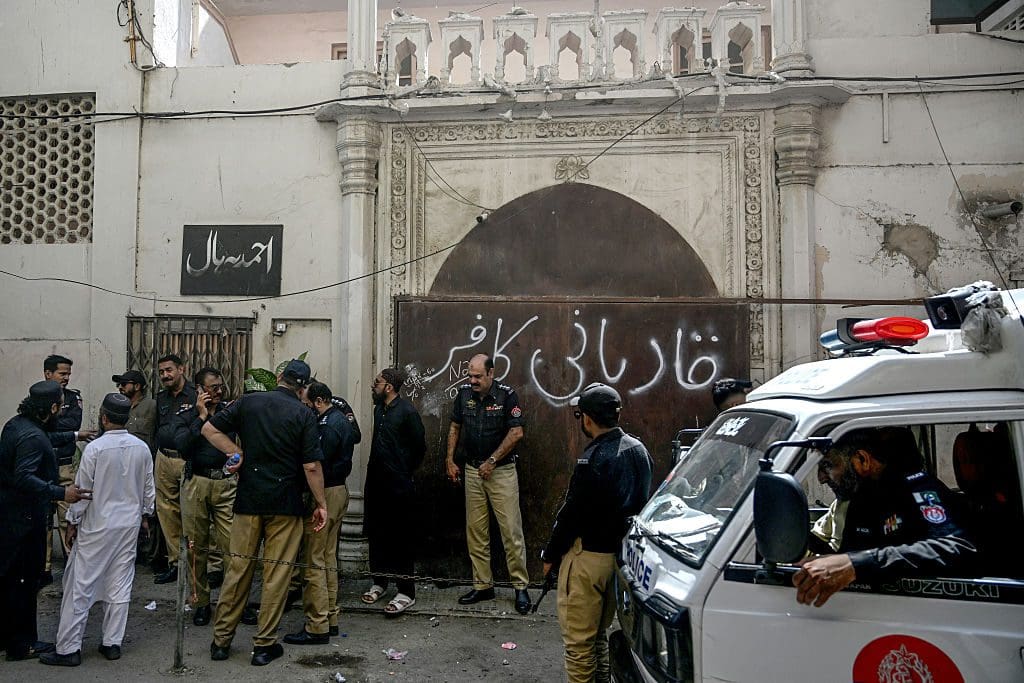 Police and a crowd stand outside a religious building painted with graffiti on its front door.