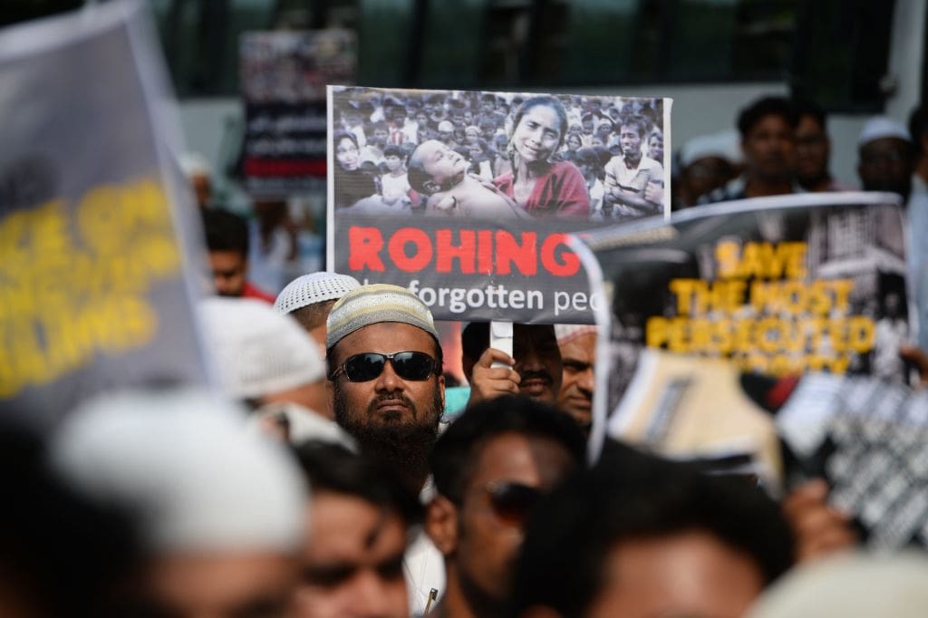 A crowd of people at a protest holding a sign that says ROHINGYA in all capital letters, with the words 