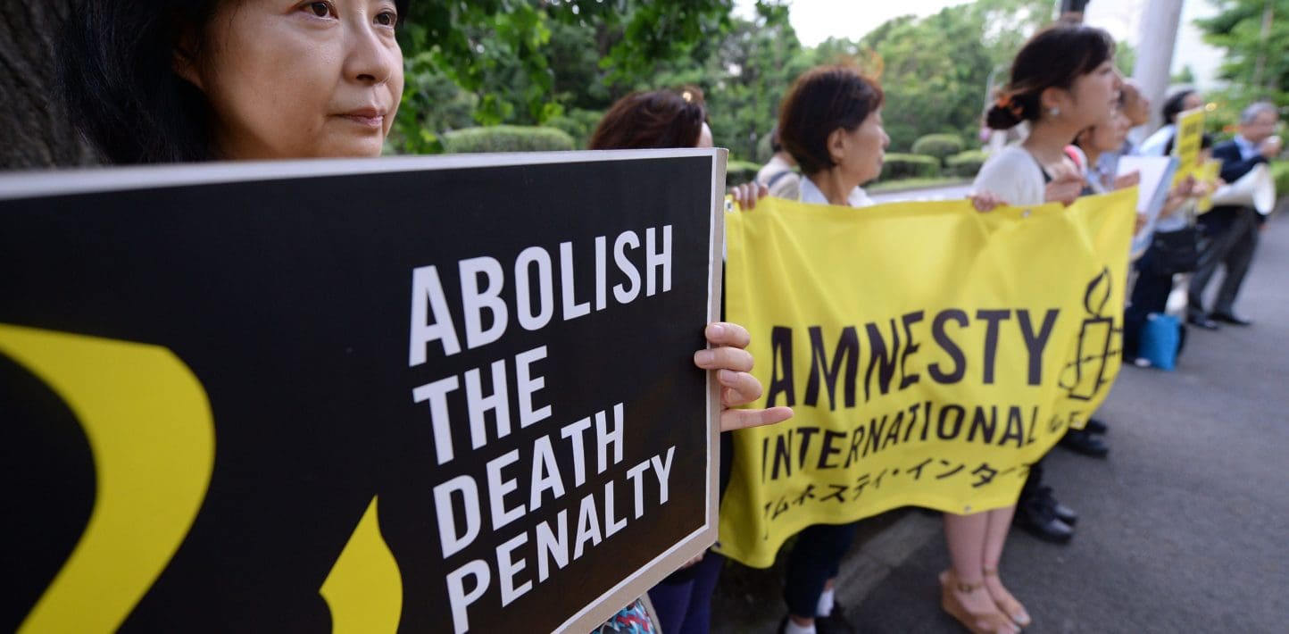 A group of people hold yellow and black banners at a protest that read