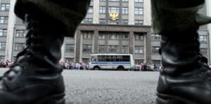 A bus and a group of people seen across a street from between two tall leather boots.