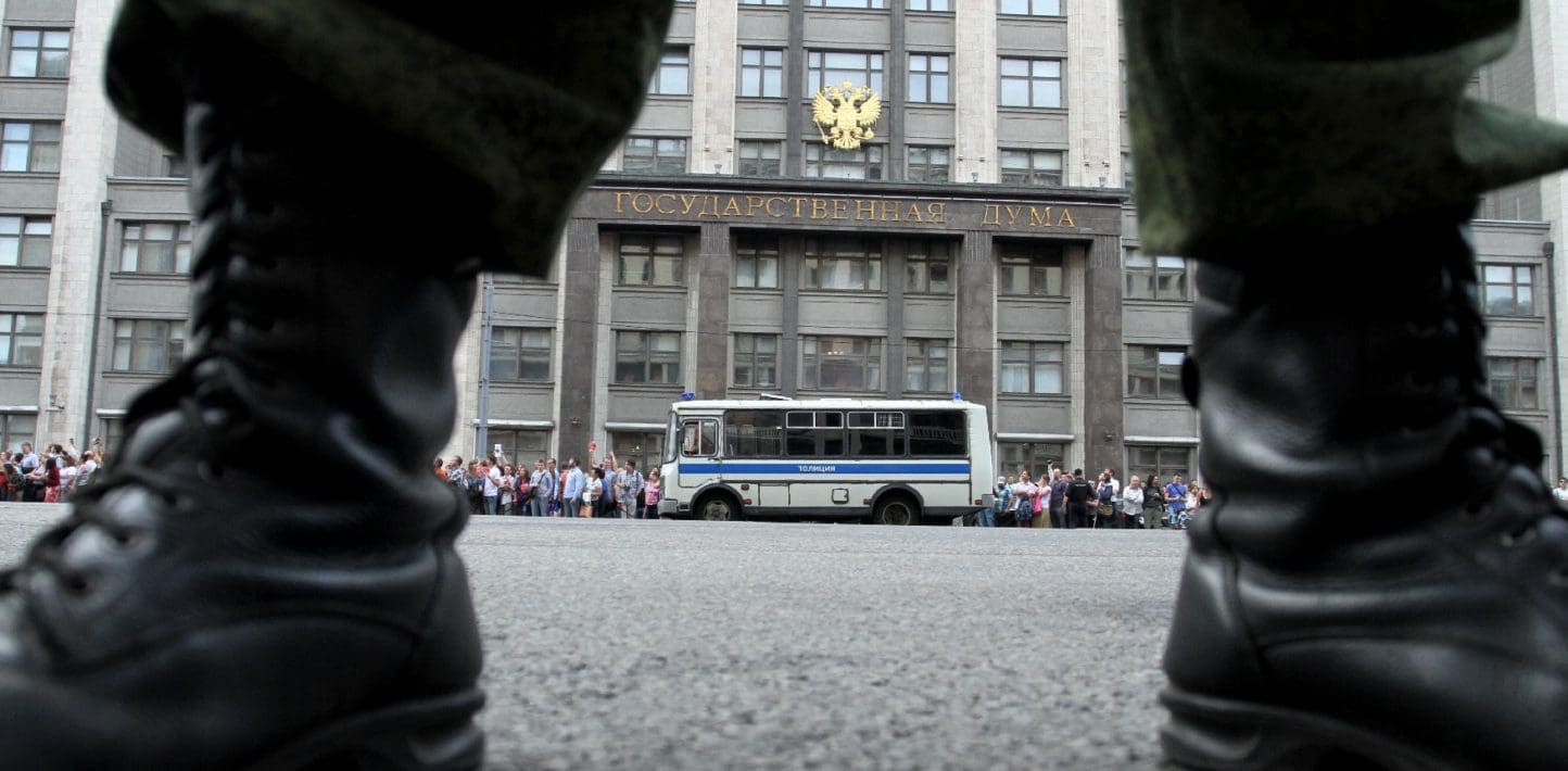 A bus and a group of people seen across a street from between two tall leather boots.