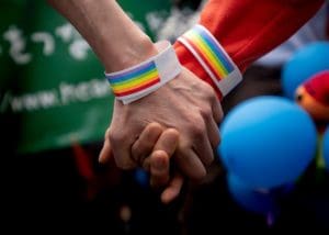 Two hands holding with rainbow wristbands in front of a balloon.