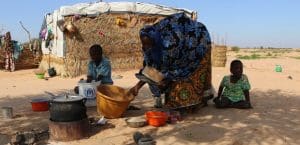 A mother with her two children depicted in a UNHCR refugee camp in the Sahel region of Africa.