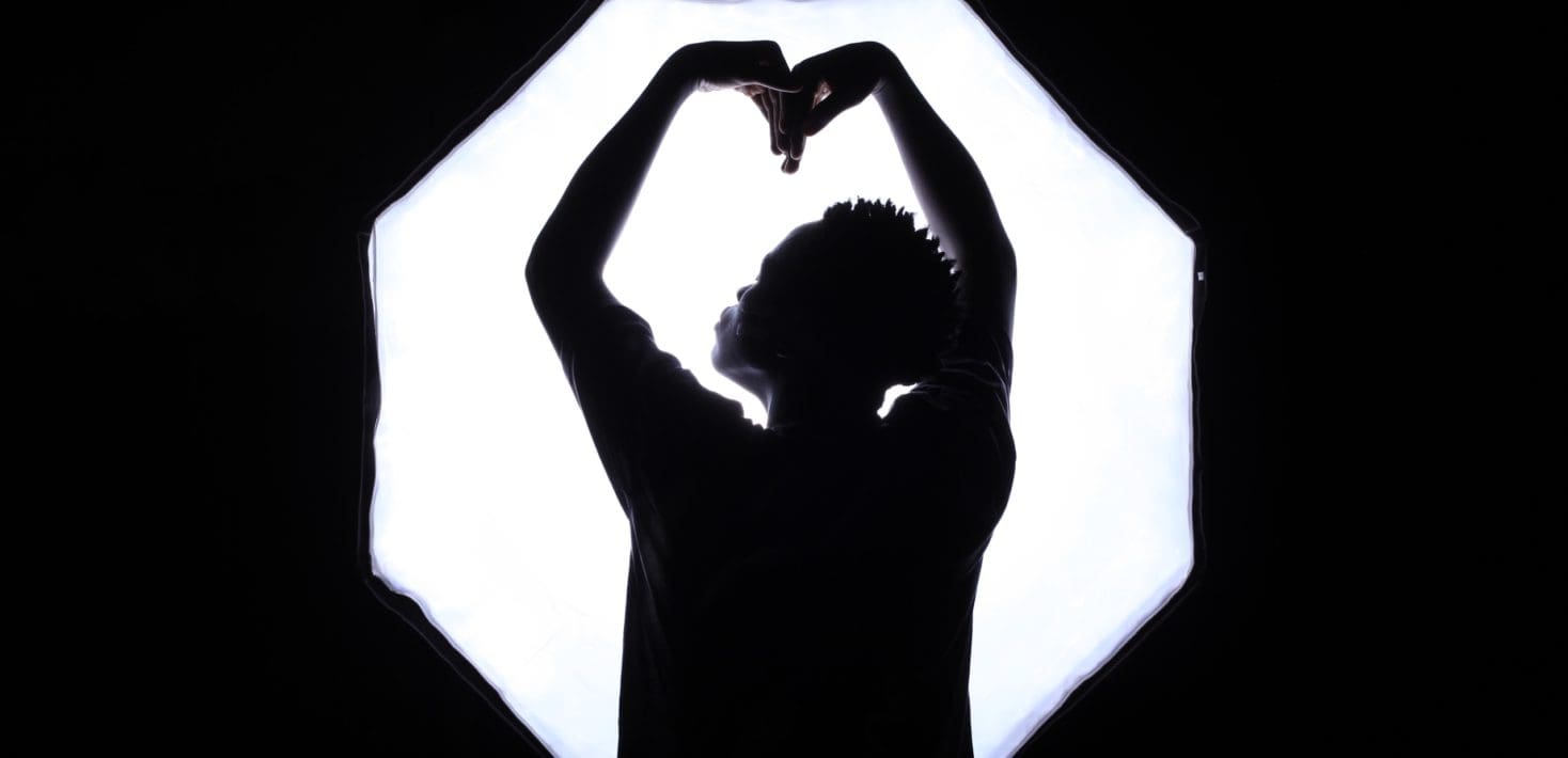 Woman standing looking away, with arms forming shape of heart.