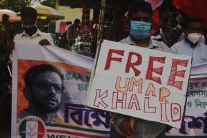 Three men wearing surgical masks hold signs reading 