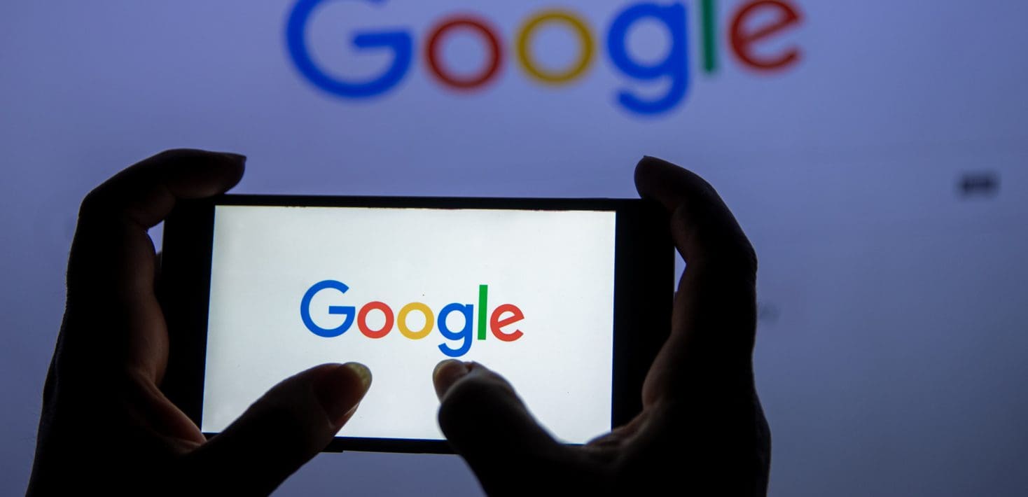 Two silhouetted hands hold a cell phone with a glowing white screen, with the word 