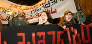Four people protesting in Georgia. They are holding protest banners and a megaphone.