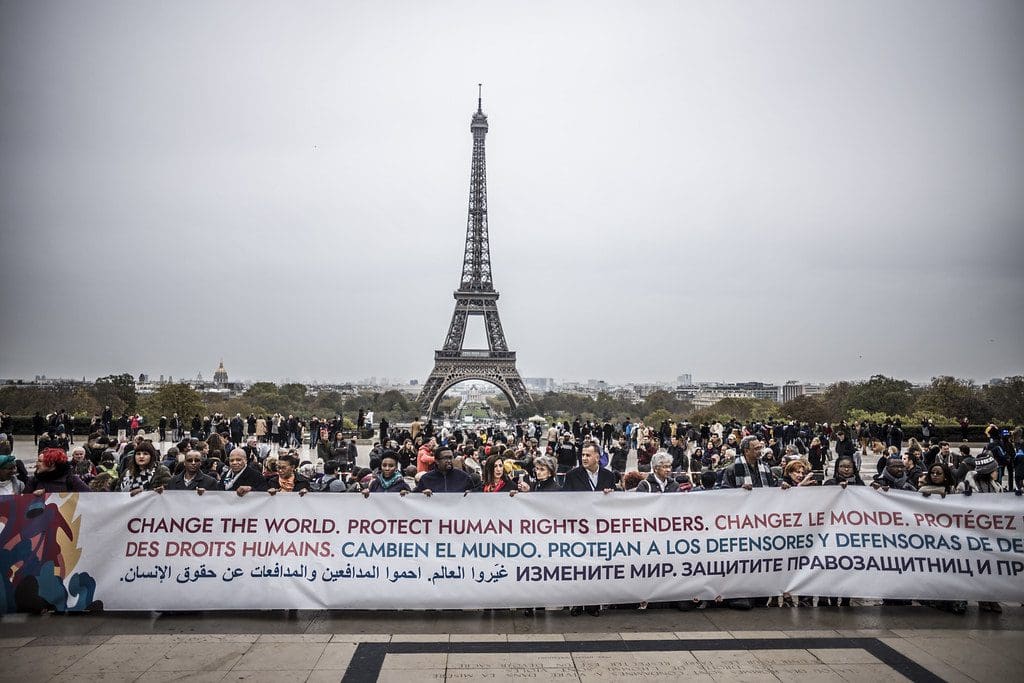 A group of people holding a protest banner in front of the Eiffel Tower.
