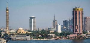 Skyscrapers of the Cairo skyline rise above trees by the Nile river.
