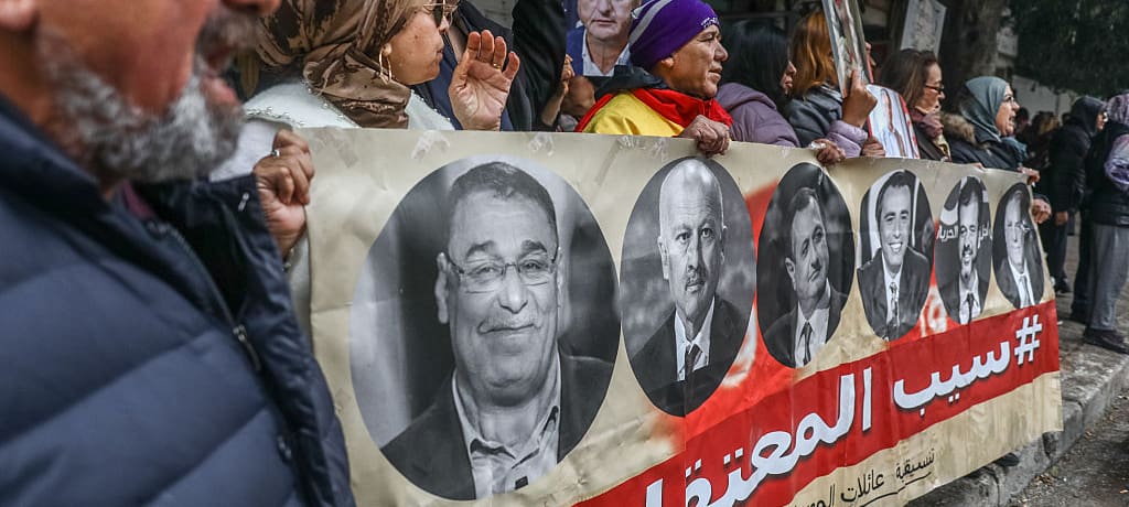 Protesters hold a banner showing the faces of imprisoned people.