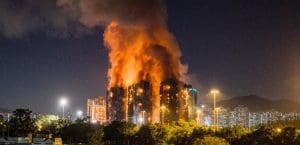 A block of apartment buildings engulfed in flames and smoke against a dark night sky.