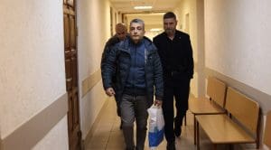 Three middle aged men walking through a hallway of a court building, One is Russian opposition politician Lev Shlosberg.