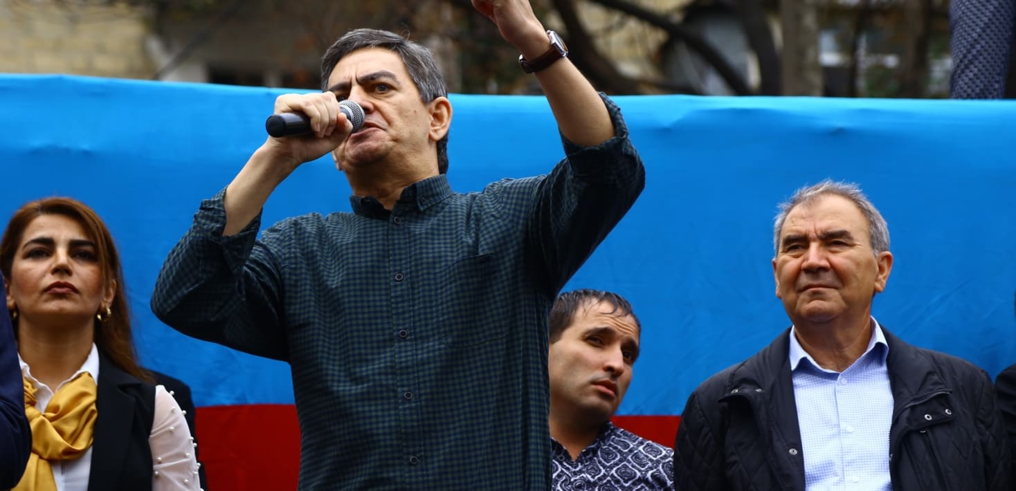 A middle aged man in a dark blue button-down shirt speaking with a microphone
