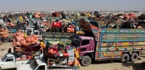 A collection of colorful buses and trucks, many of them loaded to capacity with bundles of people's belongings, stretch into the distance on a hot day.